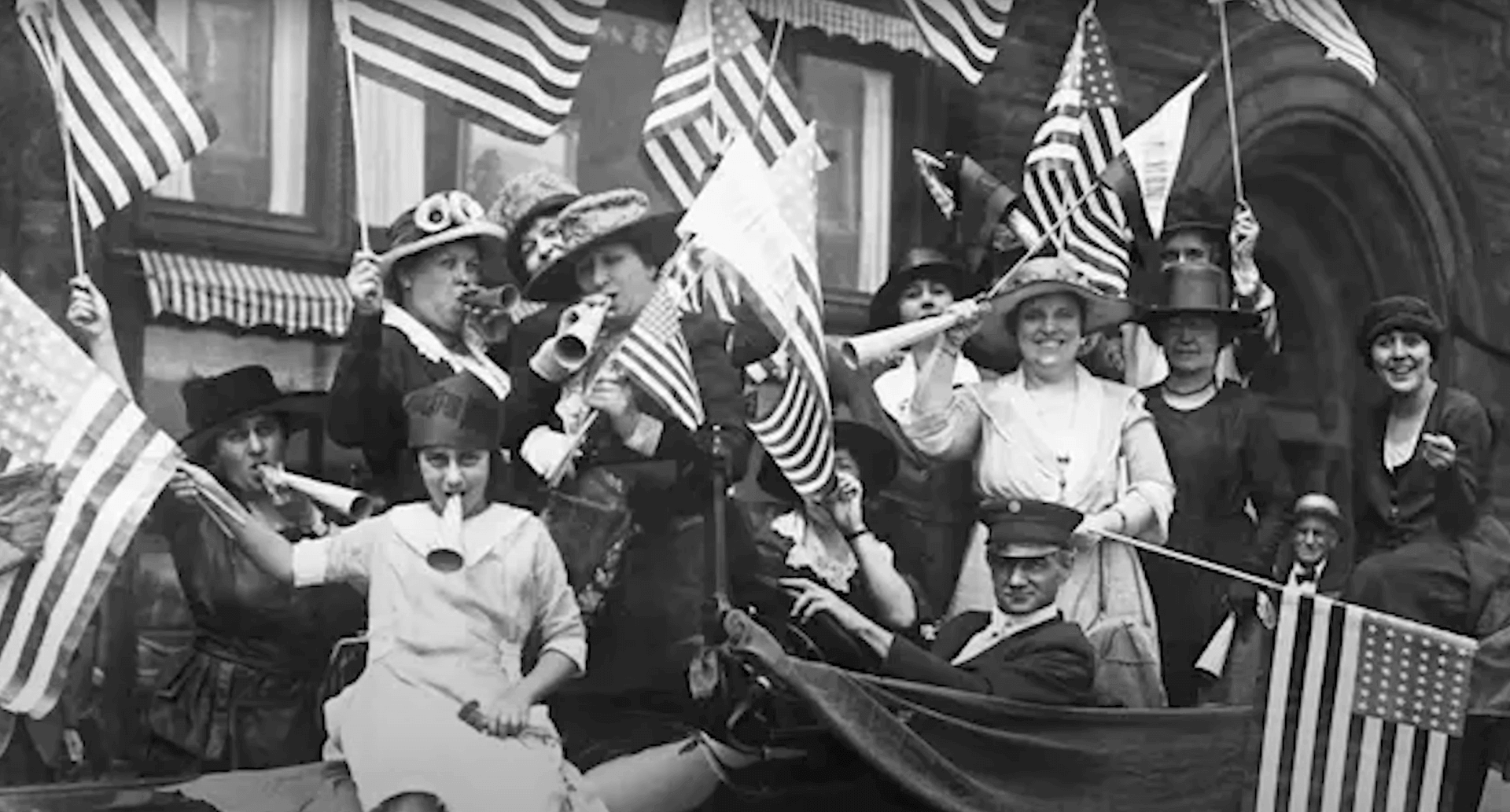 Woman speaking at a podium during a press conference with Revolutionary War reenactors in the background