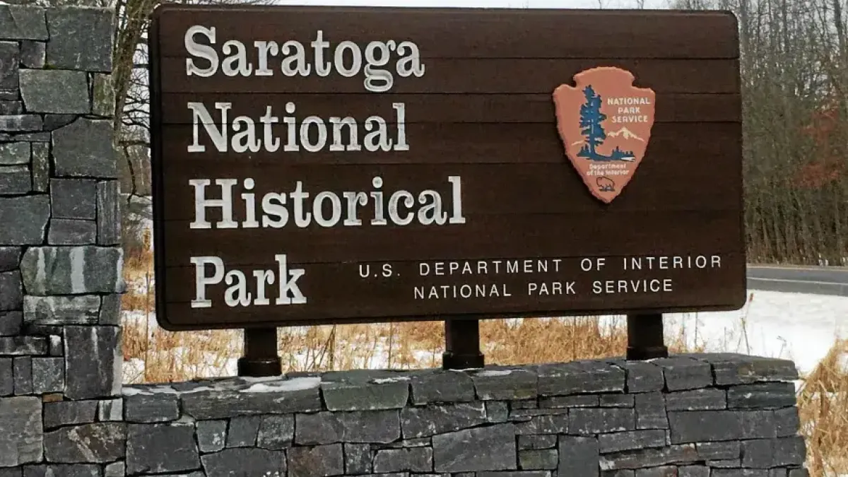 Woman speaking at a podium during a press conference with Revolutionary War reenactors in the background