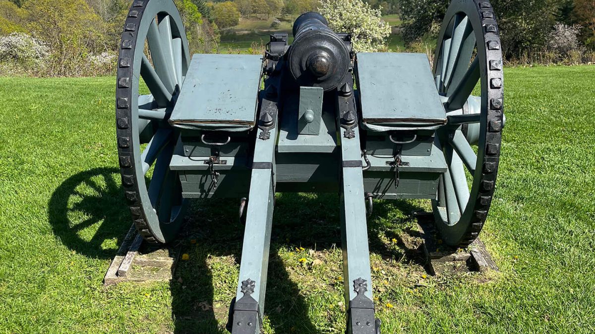 Woman speaking at a podium during a press conference with Revolutionary War reenactors in the background