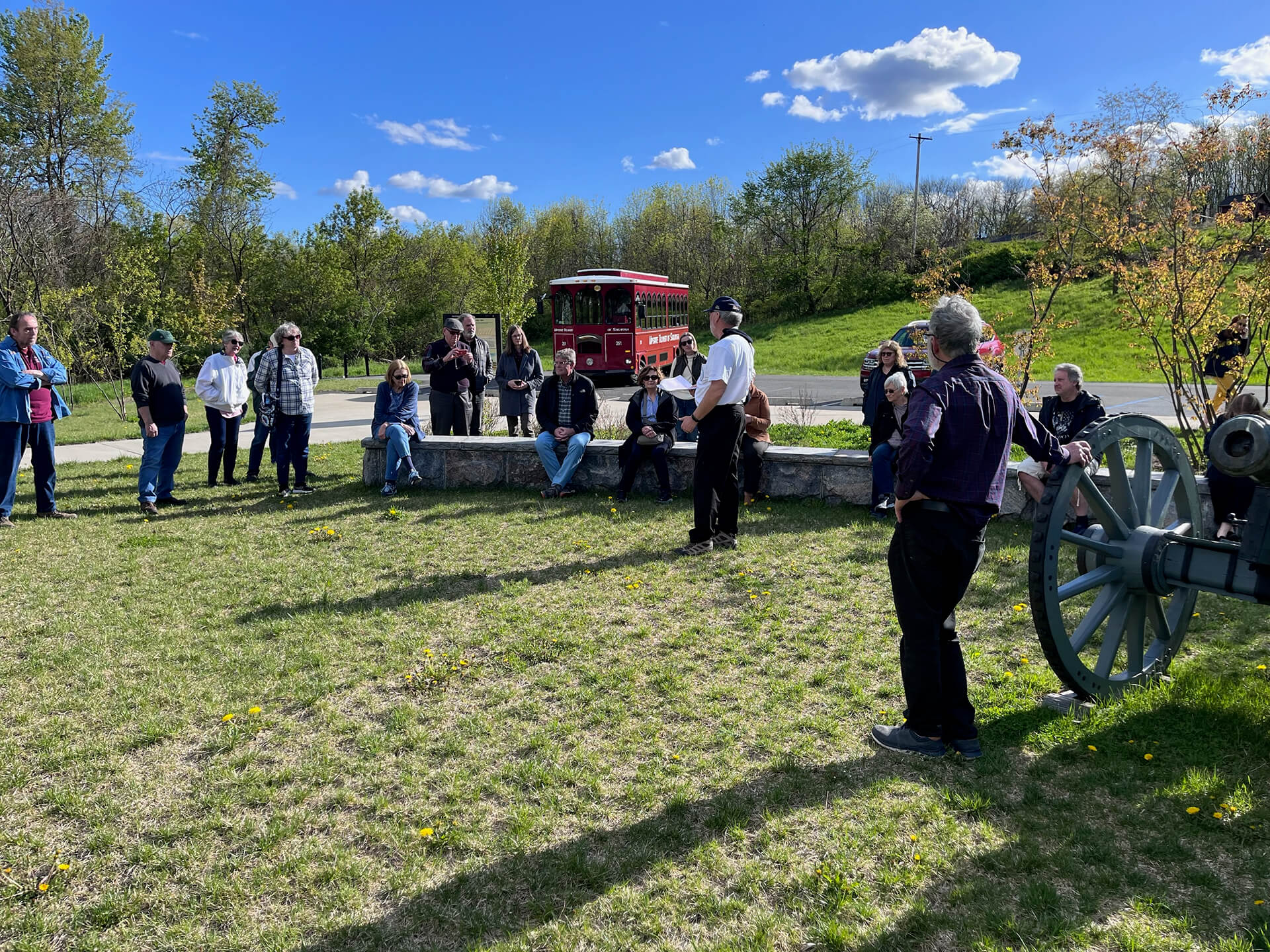 A group gathered at a historic site listening to a tour guide with a trolley in the background