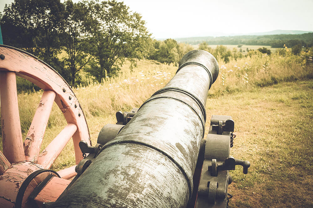 Close up of a historical cannon with fields and mountains in the background