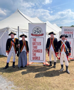 Revolutionary War reenactors standing near a sign that reads, "Battles of Saratoga 250: The battles that changed the world"