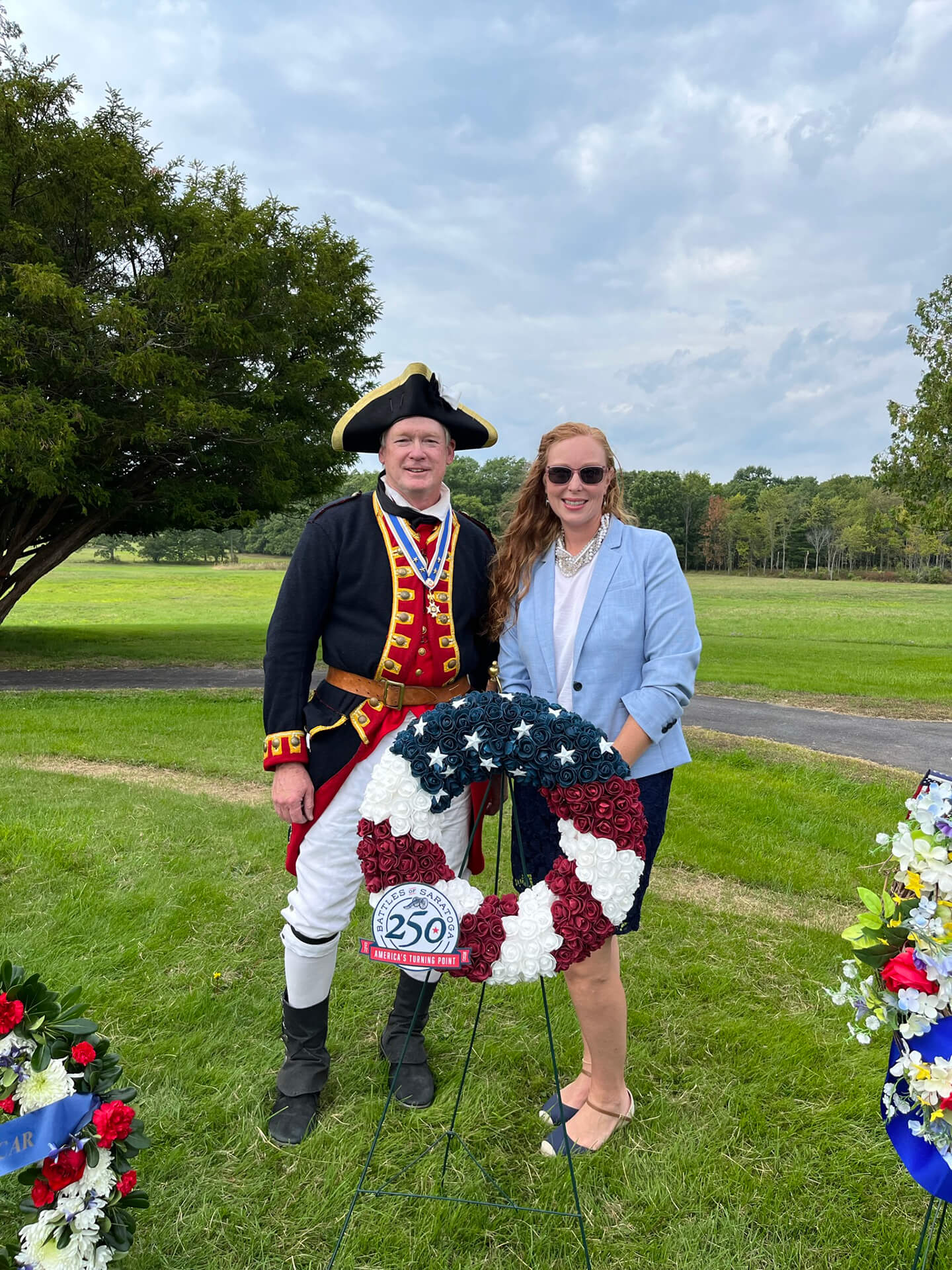 A man and woman standing behind a wreath stand decorated like the American flag