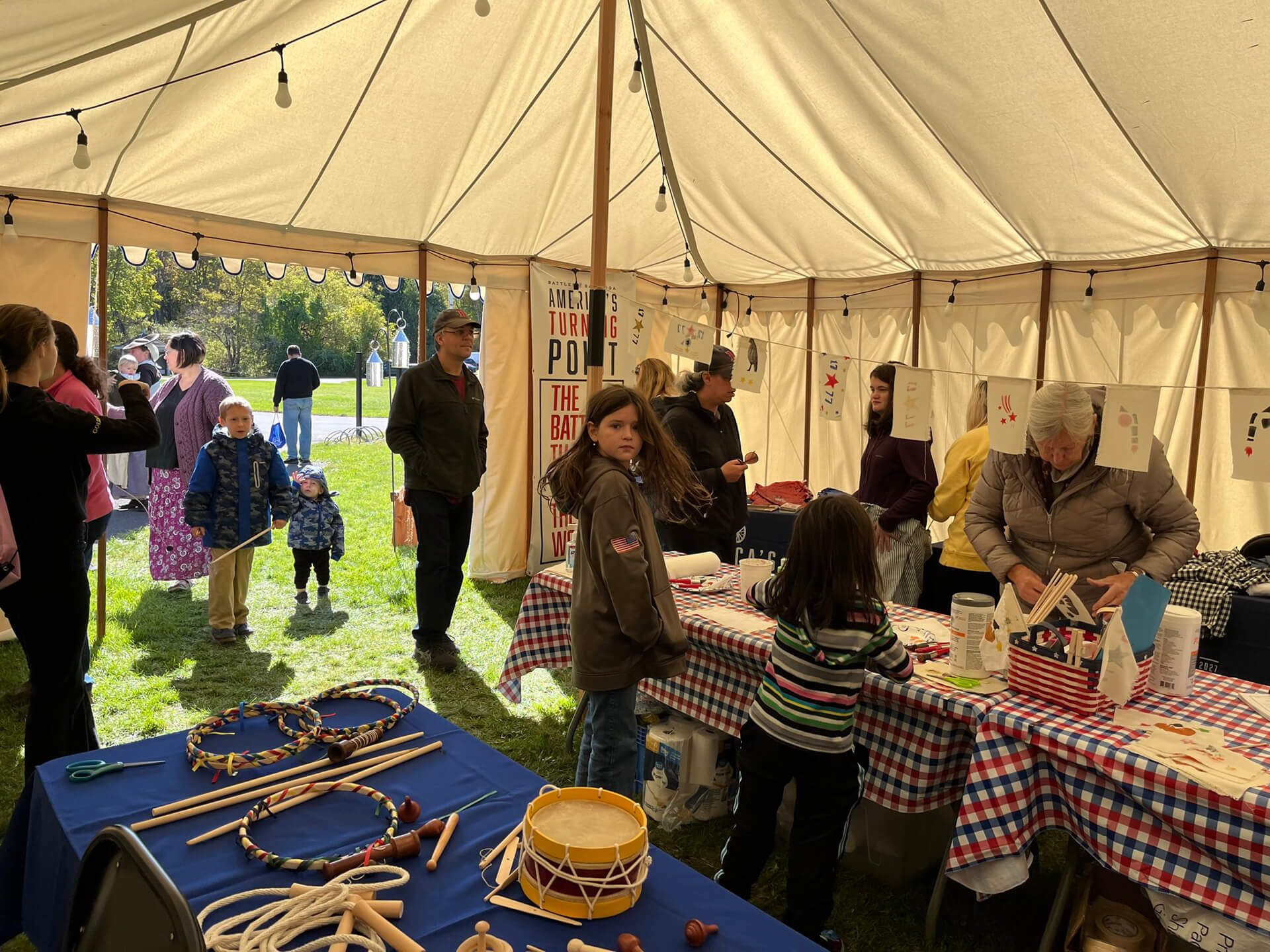 People gathered inside a Saratoga 250 tent with Revolutionary War era games and crafts