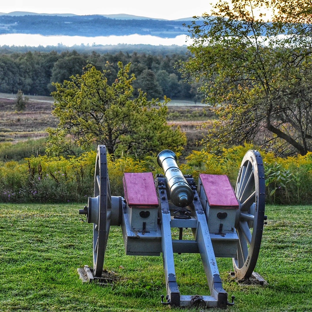 Close up of a historical cannon with fields and mountains in the background