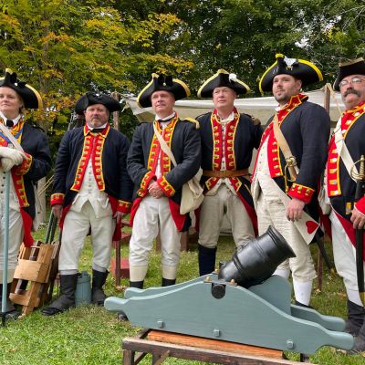 Revolutionary War reenactors near a tent with a small cannon